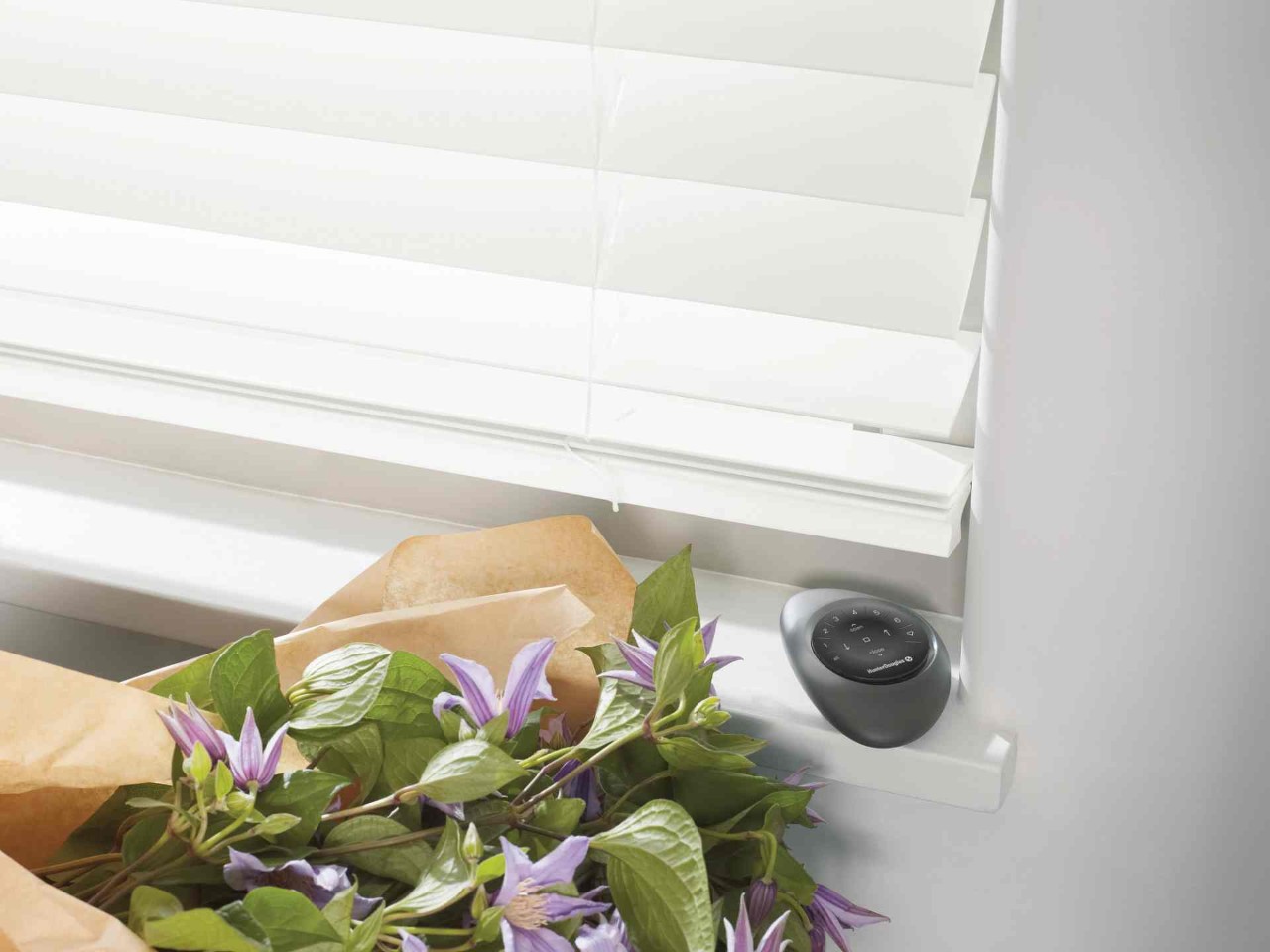 Black Pebble® Remote for the PowerView® Automation system on a window sill next to a floral bouquet  at Midwest Blind & Shade near Mishawaka, IN